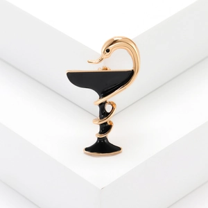 Détail de la broche médicale avec serpent doré et coupe en émail noir sur fond blanc