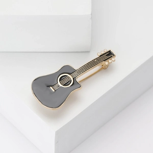 Elegant black enamel guitar brooch with gold metal accents on a minimalist white stage