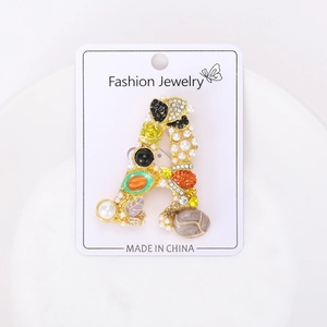 Macro detail of luxury letter A brooch with pearls, crystals and green enamel in gold
