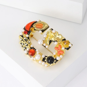 Baroque style golden letter G brooch with pearls and colorful gemstones on white background