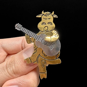 Detailansicht einer goldenen Zeichentrick-Ochse-Brosche mit Gitarre im Vintage-Stil