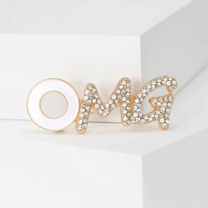 Elegant gold OMG brooch with sparkling rhinestones and white enamel inlay on a white stand