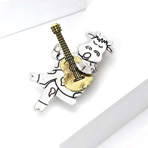 Detailansicht der Cartoon-Kuh-Brosche in Silber und Gold, die Gitarre auf Block spielt