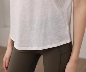 Dettaglio canotta yoga in tencel bianco con bordo curvo e tasca laterale su legging oliva