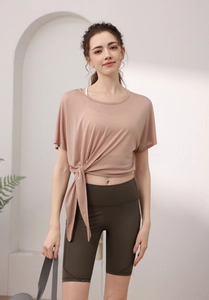 Détail du haut de yoga rose noué et du short cycliste olive avec sangle de tapis yoga