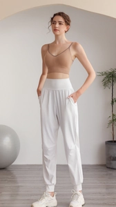 Donna in reggiseno sportivo marrone e pantaloni bianchi a vita alta in uno studio di yoga