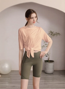Détail du t-shirt de sport noué pêche clair et du short de yoga vert olive avec poche latérale