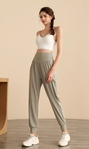 Dettaglio laterale dei pantaloni sportivi a vita alta verde salvia e canotta bianca su modella