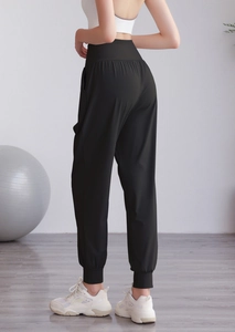 Dettaglio dei pantaloni jogger neri a vita alta con retro plissettato e polsini a coste