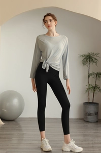 Détail d'un haut de yoga noué bleu clair et legging noir taille haute dans un studio