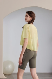 Dettaglio del top da yoga in rete gialla e pantaloncini ciclista a vita alta verde oliva