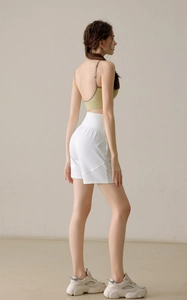 Back view of a woman wearing light green ribbed sports bra and white high-waisted gym shorts