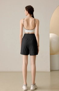 Rear view of model wearing black high-waisted loose gym shorts and white strappy yoga bra