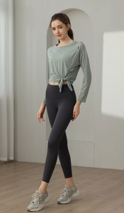 Detail of jade green tie-waist yoga top with shoulder cutout and grey leggings