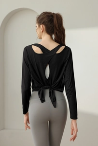 Detail eines schwarzen Yoga-Oberteils mit offenem Rücken, Kreuzgurten und grauer Leggings