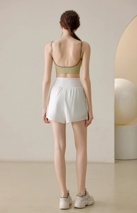 Rear view of avocado green sports bra and white loose running shorts in a minimalist room