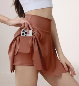 Detail of high-waisted brick red tennis skort with scallop hem and hidden phone pocket