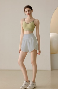 Women's avocado green sports vest and light gray yoga shorts set in a minimalist studio