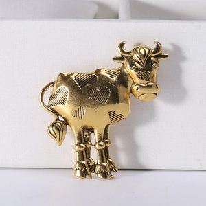 Detailed close-up of a vintage golden cow brooch with engraved heart patterns on white box