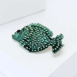 Macro view of a teal enamel fish brooch featuring detailed scale textures and dark bead eye