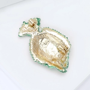 Detailed back view of a golden alloy fish brooch showing safe pin closure and green enamel edges
