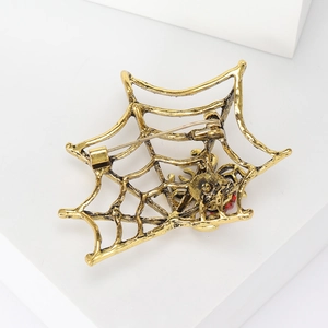 Vintage gold spider web brooch with red crystal accents on a minimalist white stand