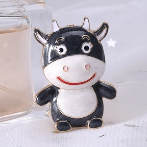 Close-up of cute cartoon cow brooch featuring black and white enamel and golden edges