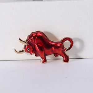 Detailed view of a red enamel bull brooch with gold accents on a white textured background