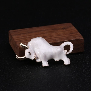 Close-up of white enamel bull brooch with gold horns on dark wood background