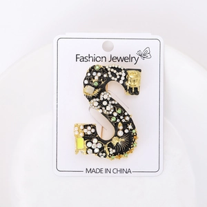 Détail macro de l'élégante broche lettre S avec émail noir, perles et cristaux