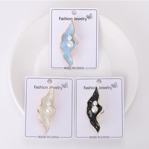 Detailed macro view of enamel leaf brooches with elegant pearls in blue, white and black