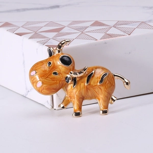 Gros plan d'une broche boeuf dorée avec émail orange marbré sur une boîte cadeau