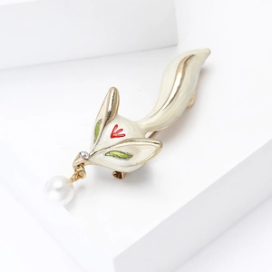 Detailed close-up of a white fox enamel brooch with gold accents and a hanging pearl