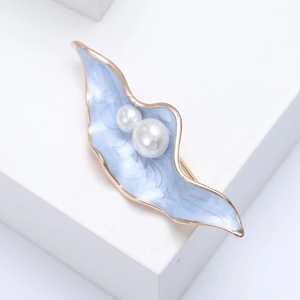 Détail d'une broche feuille en émail bleu avec double perles sur socle doré sur fond blanc