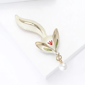 Detailed view of white enamel fox brooch with green eyes and hanging pearl drop