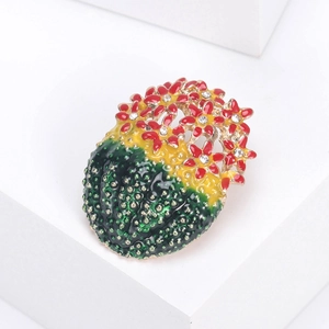 Détail d'une broche cactus en émail avec fleurs rouges et cristaux blancs sur bloc blanc