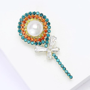 Detail of a gold lollipop brooch featuring a white pearl and colorful rhinestones