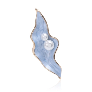 Détail macro d'une élégante broche feuille en émail bleu clair avec deux perles blanches
