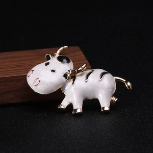 Vue détaillée d'une jolie broche vache en émail blanc et dorure sur socle en bois