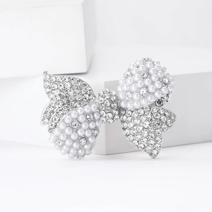 Sparkling bow brooch with silver metal, rhinestones and pearls on white background