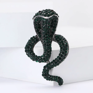 Exquisite snake brooch pin with sparkling green crystals on white geometric stand