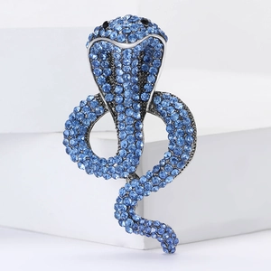 Elegant cobra snake brooch pin with blue crystals on a white geometric stand