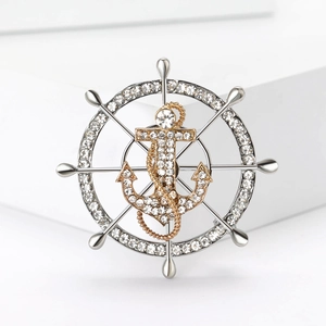 Close-up of anchor and wheel brooch with inlaid crystals and delicate metal chain details
