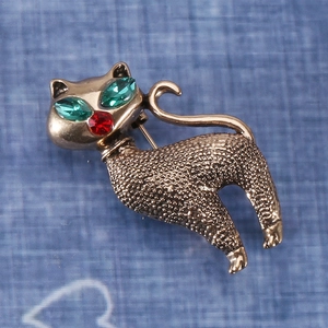Close-up of vintage cat brooch with green rhinestone eyes and bronze alloy texture