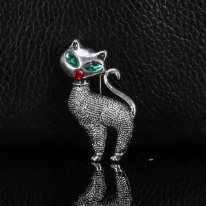 Detailed close-up of a silver cat brooch with green gem eyes and a red nose on black leather
