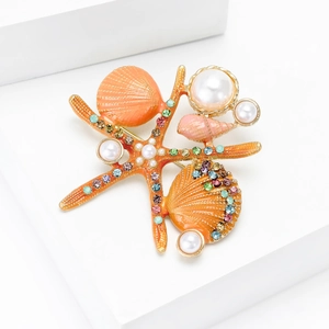 Détail de la broche étoile de mer et coquillage en émail orange avec perles et strass