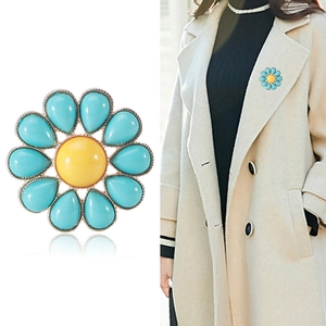 Elegante spilla a girasole dorata con petali blu e centro giallo su un cappotto