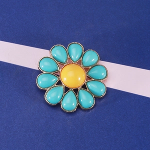 Dettaglio elegante spilla a fiore turchese con centro giallo e base in metallo dorato
