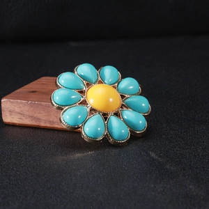 Dettaglio di un'elegante spilla a fiore verde con accenti dorati e una perla gialla centrale