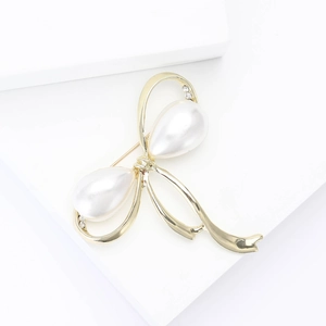 Broche nœud dorée élégante avec perles blanches et strass sur fond blanc minimaliste